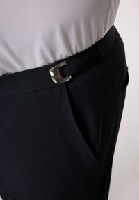 Pantaloni neri con una consistenza liscia e una fibbia in metallo argento sulla cintura. Presentano una tasca laterale e una vestibilità su misura.