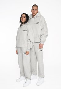 Graue Kapuzenpullover und Jogginghosen mit dem Logo "MULTIPLY APPAREL" in Schwarz. Der Stoff scheint weich zu sein mit einer lockeren Passform und elastischen Bündchen. Weiße Sneaker.