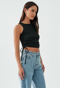 Mustat ribbed-tank topit, joissa on sivun kiristysnyörit, yhdistettynä vaaleansinisiin korkeavyötäröisiin farkkuihin. Yksinkertainen muotoilu, jossa on istuva siluetti.
