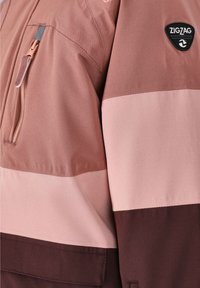 En brun och rosa randig jacka i mjukt material, med en dragkedjeförsedd ficka och en logotyp på överarmen.
