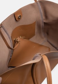Tan leren totebag met een gladde buitenkant, voorzien van een zachte suède voering, interne vakken en een klein ritsvakje.