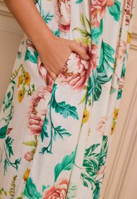 Robe à motif floral mettant en avant de grandes pivoine roses et jaunes sur un fond blanc, avec une poche sur le côté et un tissu doux et texturé.