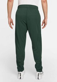 Pantalones deportivos de color verde oscuro con cinturilla elástica, bolsillos laterales y piernas ajustadas con cremalleras en los tobillos.