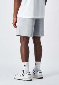 Graue Sportshorts mit lockerem Schnitt, kombiniert mit weißen Socken mit Logo und klobigen weißen Turnschuhen mit marineblauen Akzenten.