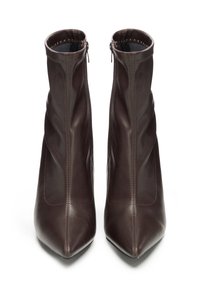 Pár tmavě hnědých kožených kotníkových bot s špičatými špičkami a bočními zipy, zobrazených vzpřímeně na bílém pozadí.