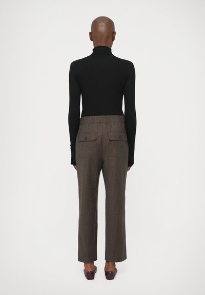 Pulover negru cu mânecă lungă și guler înalt, asortat cu pantaloni maro texturați, ce au un croi lejer, talie elastică și două buzunare la spate.