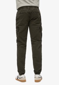 Donkergroene cargobroek met elastische enkels, meerdere zijzakken en een relaxte pasvorm. De stof lijkt stevig en lichtgewicht.