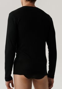 Czarna longsleeve w miękkim materiale z okrągłym dekoltem, dopasowanym fasonem i płaskimi szwami, noszona z czarnymi slipami.
