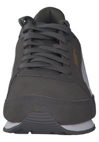 Tmavě šedé tenisky Puma s tlustými tkaničkami, semišovým svrškem, bílou podrážkou a zlatým logem Puma na boku, viděné zepředu.