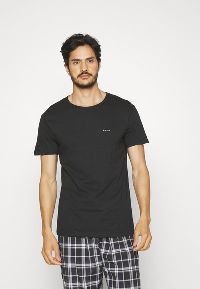 Camiseta de algodón negra con cuello redondo y mangas cortas, con un pequeño logo blanco en el pecho; combinada con pantalones de pijama a cuadros.