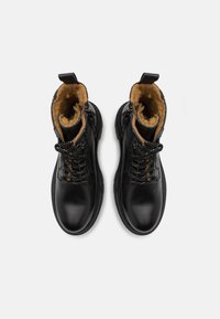 Bottines en cuir noir avec surface texturée, doublure en fourrure, lacets contrastés et tirette à l'arrière. Semelles en caoutchouc antidérapantes.