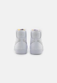 Bílé vysoké tenisky z hladké kůže, s polstrovaným límcem a jemným embosovaným logem "Nike" na zadní straně. Gumová podešev s texturovaným gripem.