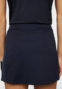 Marinblå idrotts kjol med en slät yta, prydd med en broderad logo på midjan och en rak fåll.