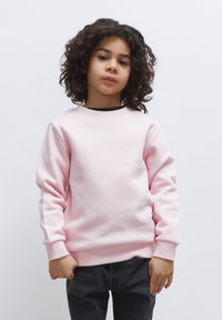 Felpa rosa chiaro con collo rotondo e polsini a costine, abbinata a pantaloni grigi scuri. Tessuto morbido, progettata per un look informale.