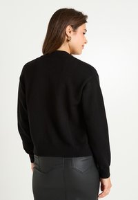 Pull noir avec un col arrondi, des manches longues et des poignets et un ourlet côtelés. Le tissu semble doux avec une texture lisse. Vue de dos.