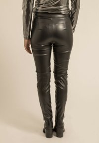 Pantalons noirs en simili cuir taille haute, à coupe slim, avec une texture lisse, des détails de couture minimalistes et des zippers aux chevilles.