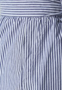 Modrý a bílý pruhovaný materiál s tenkými vertikálními liniemi, nabíranou strukturou a viditelnými švy. Materiál se jeví jako lehký.