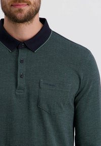 Langsleeve polo shirt in donkergroen met een visgraatpatroon, marineblauwe kraag, drie knopen en een borstzak. Geweven stofafwerking.