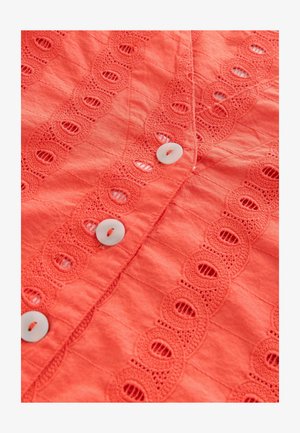 Korall színű gombos ing, texturált anyagból, csipkeborítással, körkivágásokkal és fehér gombokkal az eleje mentén.