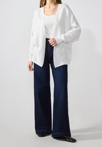 Vit, lätt öppen cardigan med långa ärmar, matchad med högmidjade mörkblå jeans med vida ben och svarta lägenheter.