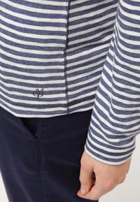 Maglietta a maniche lunghe con righe orizzontali blu e bianche, realizzata in un tessuto testurizzato. Include un piccolo dettaglio con logo sull'orlo.