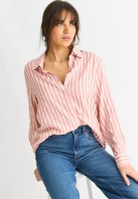 Light pink and white striped button-up shirt with a relaxed fit, featuring a collar, long sleeves, and a button placket. Paired with blue jeans.
