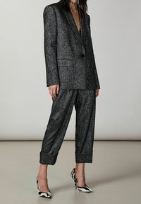 Donna che indossa un blazer oversize grigio scuro scintillante abbinato a pantaloni con risvolto e décolleté a righe bianche e nere.