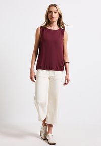 Top sin mangas burdeos con hombros fruncidos, combinado con pantalones de pierna ancha blancos y zapatillas beige. Tejido suave y corte holgado.