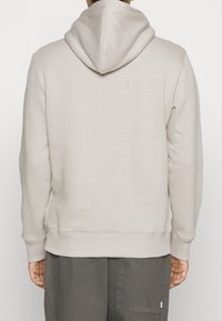 Světle béžová mikina s prostornou kapucí, žebrovanými manžetami a lemem. Vyrobena z měkké látky, má minimalistický design a neobsahuje viditelné loga.