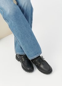 Mustadast mustad nahast kingad ümmardatud toe ja tekstuuriga tallaga, kuldsete silmade ja paeltega, koos helesiniste denim pükstega.