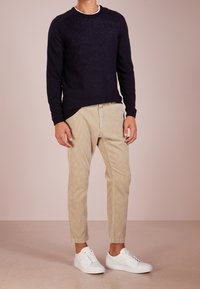 Marineblauer Strickpullover mit einem gerippten Rundhalsausschnitt, kombiniert mit hellbeigen Cordhosen und weißen Low-Top-Sneakern. Glatte Textur und taillierter Stil.