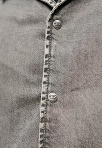 Κοντινή λήψη γκρι τζιν ύφανσης με δύο μεταλλικά κουμπιά χαραγμένα με τη λέξη «DIESEL» κατά μήκος της ραμμένης ραφής.