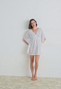 White lace cover-up with a V-neck, loose sleeves, and an ankle-length hem, featuring intricate patterns and a lightweight texture.