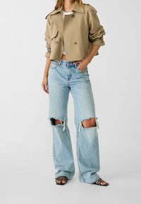 Beżowy krótki płaszcz typu trencz z podwójnym rzędem guzików, połączony z jasnoniebieskimi, szerokimi dżinsami z dużymi przetarciami na kolanach. Czarne klapki na płaskiej podeszwie.