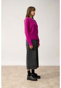 Pull en tricot fuchsia à manches longues, décolleté rond ; accompagné de culottes en denim noir taille haute et de chaussures à lacets noires.