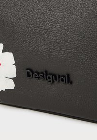 Portafoglio in finta pelle nera con superficie testurizzata, un design floreale bianco e un logo "Desigual" in rilievo di colore nero.