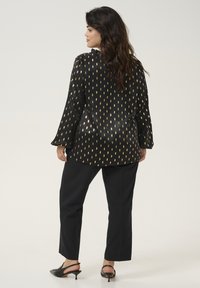 Black blouse with gold teardrop pattern, long sleeves, and loose fit. Paired with black trousers and black slingback heels.