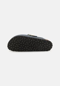 Sandaali sinisellä yläosalla, ruskeilla yksityiskohdilla ja teksturoidulla mustalla kumipohjalla, jossa on aallokkomainen kuvio liukastumisen estämiseksi. Flip-flop-tyylinen muotoilu.