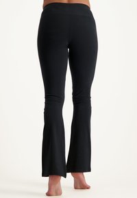 Mustat levenevät housut venyvästä kankaasta. Ominaisuuksiin kuuluu korkea vyötärö ja sileä pinta, sekä levenevät lahkeet, jotka ulottuvat nilkkoihin.