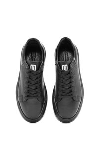 Een paar zwarte leren sneakers met zwarte veters en het witte logo op de tong, bekeken van bovenaf op een witte achtergrond.