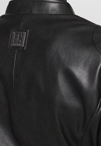 Czarna skórzana kurtka o gładkiej fakturze, z wyrazistym kołnierzem i prostokątną łatą z logo na plecach.
