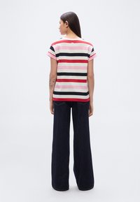 Ριγέ μπλουζάκι με κοντά μανίκια σε ροζ, κόκκινο και ναυτικό μπλε με στρογγυλή λαιμόκοψη· συνδυασμένο με φαρδιά, σκούρα τζιν παντελόνια.