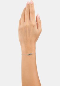 Bracciale in argento con tre piccoli gemme blu e verdi, posizionato su un polso con pelle leggermente abbronzata.