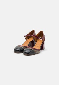 Escarpins T-strap en cuir verni noir avec un dessus texturé et coloré, présentant un talon épais et un bout rond. Détail de boucle ajustable.