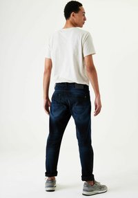 Camiseta gris claro para hombre, vaqueros azul oscuro, con los puños remangados en los tobillos, y zapatillas grises. Tejido suave con un ligero desgaste en los vaqueros.