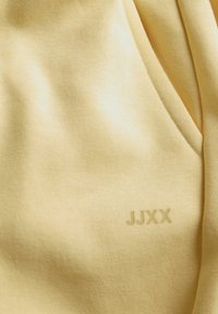 Myk gullduk med en glatt tekstur, med en subtil "JJXX"-logo trykt i en litt mørkere nyanse.