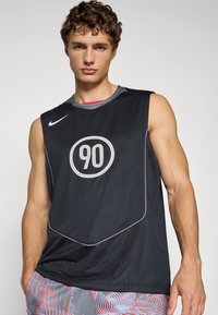 Mustaton sleeveless urheilu paita, jossa on verkkomateriaalia. Rinnassa on suuri valkoinen "90" -grafiikka ja Nike-logo. Korostettu vaaleanharmaalla reunuksella.