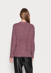 Knitted sweater in mauve with a textured leaf pattern, round neck, and ribbed cuffs. Worn with black wide-leg pants.