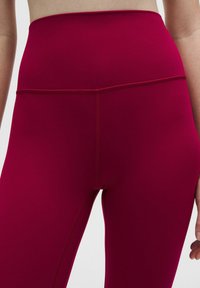 Magenta színű, magas derekú leggings sima, rugalmas textúrával; lapos derékrésszel és minimális varrási részletekkel rendelkezik.