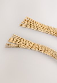 Gold-toned decorative strands with a textured, braided design, arranged in two clusters on a light background.